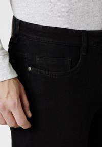 Black denim jeans with a slim fit, showing a front pocket, textured fabric, and silver hardware accent near the pocket.