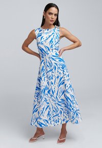 Maxi dress in white with blue abstract patterns. Sleeveless design with a boat neckline. Smooth fabric and a flowing, A-line silhouette.