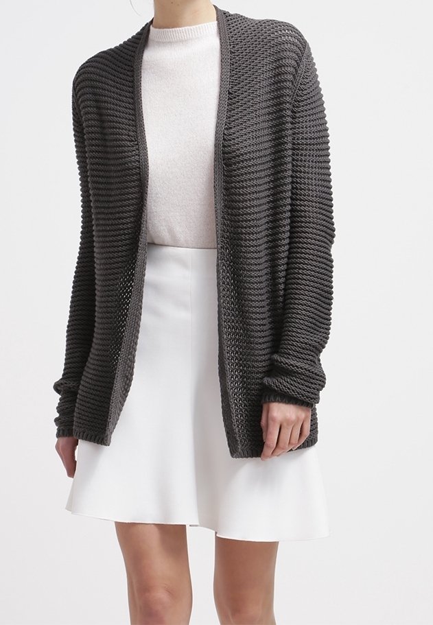 Femme portant un cardigan ouvert en maille côtelée gris foncé sur un pull blanc à col rond et une jupe évasée blanche.