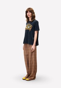 Zwart graphic t-shirt met een panterprint kroonontwerp, gecombineerd met bruine geruite wijde broek en geel-accentueerde schoeisel.