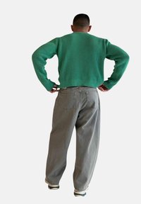 Zielony sweter z dzianiny o prążkowanej fakturze, w zestawie z jasnoszarymi spodniami o szerokich nogawkach, z tylnymi kieszeniami i luźnym krojem.