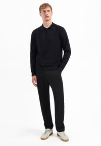 Zwarte kwart-rits pullover met raglanmouwen, zachte textuur, gecombineerd met zwarte broeken en witte sneakers met gestructureerde accenten.