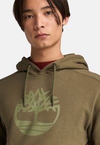 Felpa verde oliva con un grande logo ad albero a contrasto. Progettata con cappuccio regolabile e tessuto morbido per il massimo comfort.
