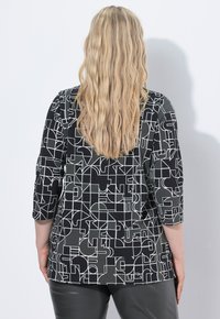 Mustapukun ja harmaan yläosan, jossa on kolme neljäsosapituista hihaa ja geometrinen valkoinen viivoituskuvio. Sujuva kangas, jossa on rento istuvuus.