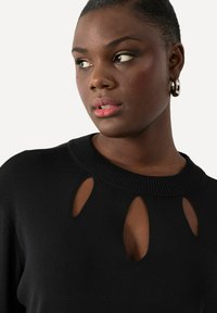 Pull en maille noire avec un col côtelé et plusieurs découpes en forme de clé à l'avant. Texture douce, design ajusté.