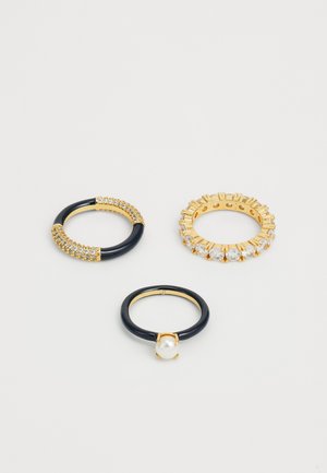 Three rings: one with black band and gold accents, one with pearl, and a gold band set with clear crystals and textured edges.