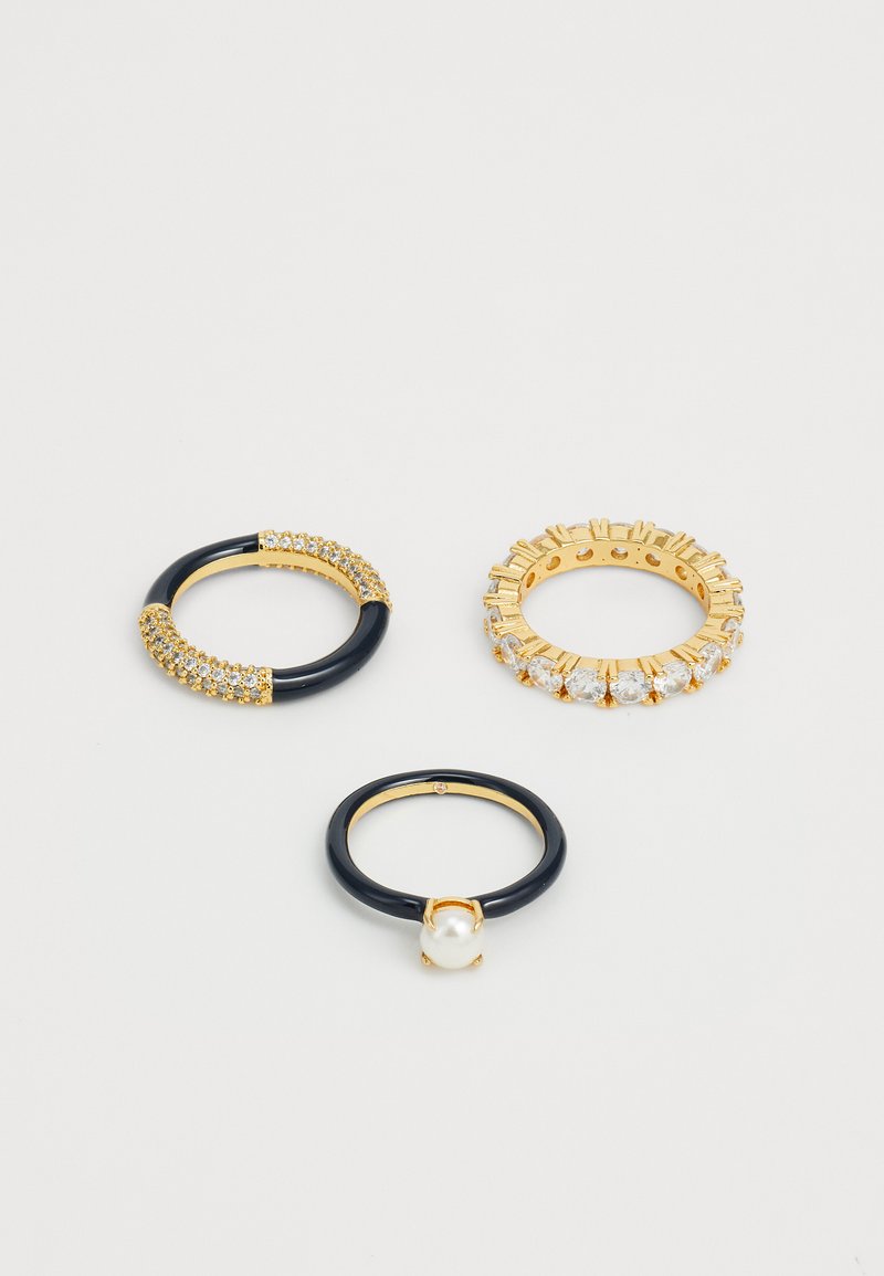 Three rings: one with black band and gold accents, one with pearl, and a gold band set with clear crystals and textured edges.