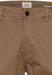 Schmale braune Baumwollhosen mit Knopfverschluss. Merkmale sind kontrastierende Nähte und normale Taschen für Funktionalität.