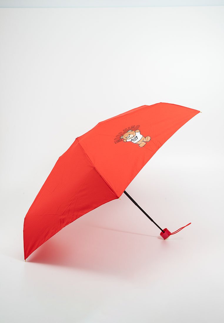Roter Regenschirm aus Stoff mit einem schwarzen Griff. Auf einer Seite befindet sich ein Cartoon-Bären-Motiv mit dem Text "MOSCHINO TOY".