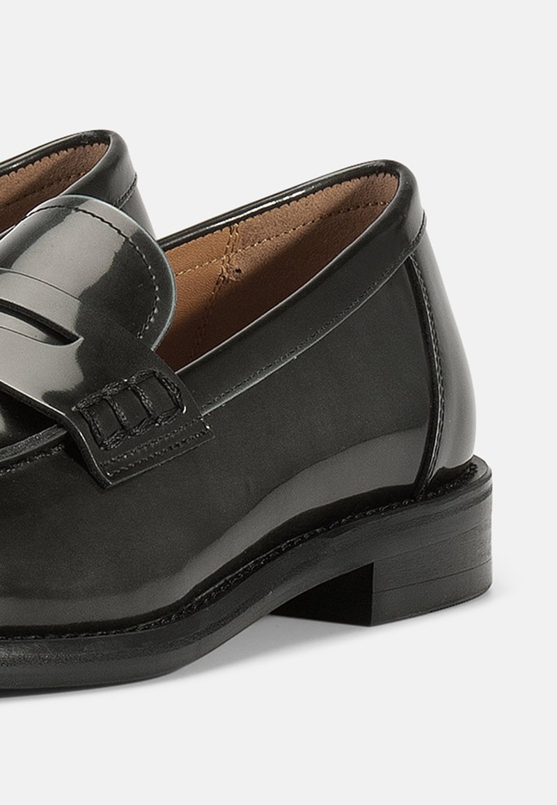 Schwarze Lackleder-Slipper mit glatter Oberfläche, dekorativem Riemen und Nähten sowie einem niedrigen Holzabsatz.