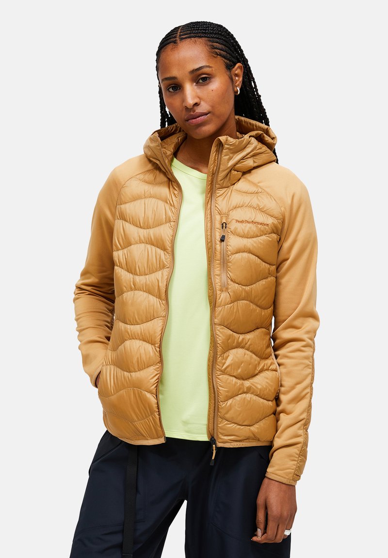 Lichte tan kleurige zip-up jas met gevoerde delen, een capuchon en zijzakken, gedragen over een felgroen shirt, gecombineerd met donkere broek.