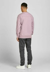 Ljust rosa sweatshirt med rund hals och ribbade ärmslut, kombinerad med mörkgrå tapered byxor och vita sneakers. Enkelt, minimalistiskt design.