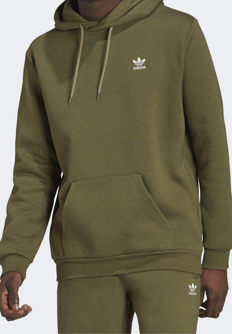 Olivově zelená mikina s kapucí z měkké látky, vybavená klokáním kapsou, stahovací kapucí a bílým logem Adidas na hrudi.