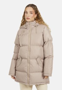 Jasno beżowa kurtka puchowa z zamkiem błyskawicznym, kapturem ze sznurkiem, dwoma bocznymi kieszeniami i pikowanym wzorem, o długości do kolan.