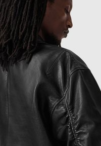 Czarna skórzana kurtka o gładkiej fakturze, lekko błyszcząca, z usztywnionymi rękawami i widocznymi detalami szwów.