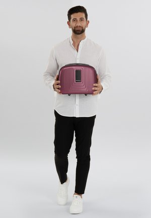 Paarse harde rugzak met geribd ontwerp, zwarte accenten en een frontpaneel, vastgehouden door een persoon in een wit shirt en zwarte broek.