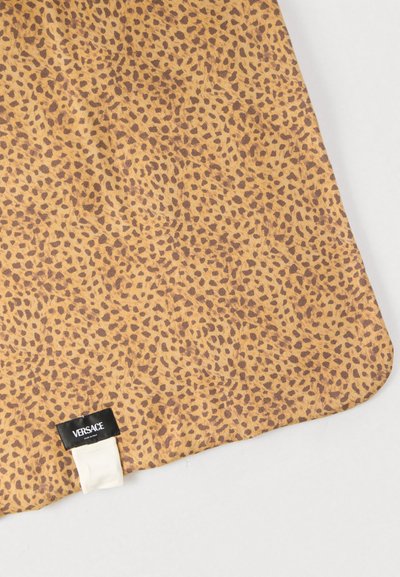 Υφαντό με μοτίβο λεοπάρ σε αποχρώσεις ανοιχτού και σκούρου καφέ, με μαύρη ετικέτα που φέρει το όνομα της μάρκας "VERSACE" σε λευκό.