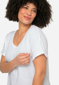 Witte T-shirt met korte mouwen, een ronde hals, zachte textuur en opgerolde mouwen. Het heeft een lichte stof en een relaxte pasvorm met subtiele draping.