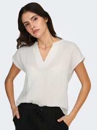 Witte, lichte, gestructureerde blouse met korte mouwen en een V-hals, gecombineerd met zwarte broek met trekkoord in de taille.