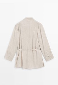 Light beige long-sleeve linen jacket with collar, buttoned cuffs, back pleats, and thin belt tied around the waist.