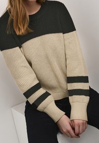 Pull en tricot beige et vert foncé, avec des rayures horizontales, un col rond côtelé et des manches longues texturées.