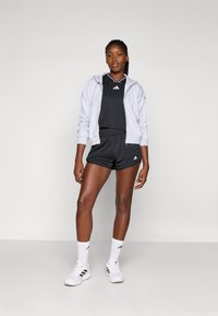 Svart treningsgenser og shorts med en grå hettejakke med glidelås, hvite sokker og sko med tre svarte striper. Jevne, lette materialer.