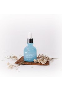 Blue glass dropper bottle with a white dropper cap, labeled "Original Skin Energy Hyaluronic Acid," placed on a woven mat with dried flowers.