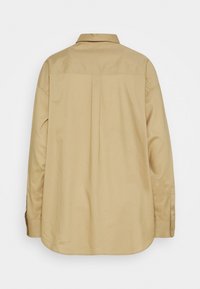 Chemise kaki à manches longues avec col, coupe droite et manches boutonnées. Texture lisse et pli creux au dos.