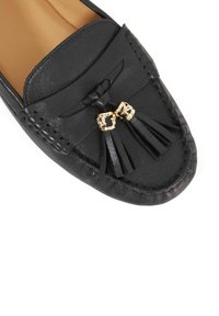 Black leather loafer with a woven detail on the toe, featuring two gold-tone buckle accents and black tassels. Smooth texture.
