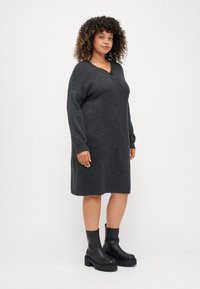 Charcoal gray oversized sweater dress with a V-neckline and long sleeves, featuring a textured knit finish. Worn with black platform ankle boots.