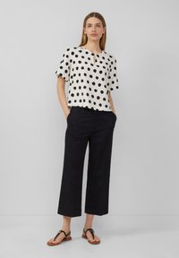 Haut blanc à manches courtes avec des pois noirs et un décolleté en trou de serrure, associé à un pantalon noir ample et des sandales plates.