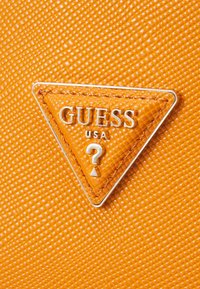 Pomarańczowy, teksturowany materiał z trójkątnym logo Guess USA wykonanym ze srebrnego metalu i detalem w kształcie znaku zapytania.