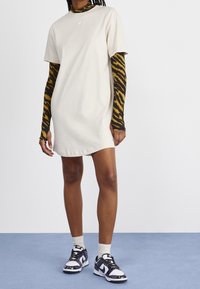 Vestido de camiseta beige claro con mangas cortas y cuello redondo, combinado con una camiseta de manga larga a rayas de tigre y zapatillas negras con estampado.