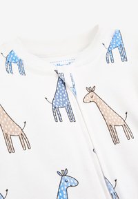Hvid body med blå og brune giraffemønstre, polka prikker og konturerede detaljer. Blødt, glat stof med lynlås lukning.