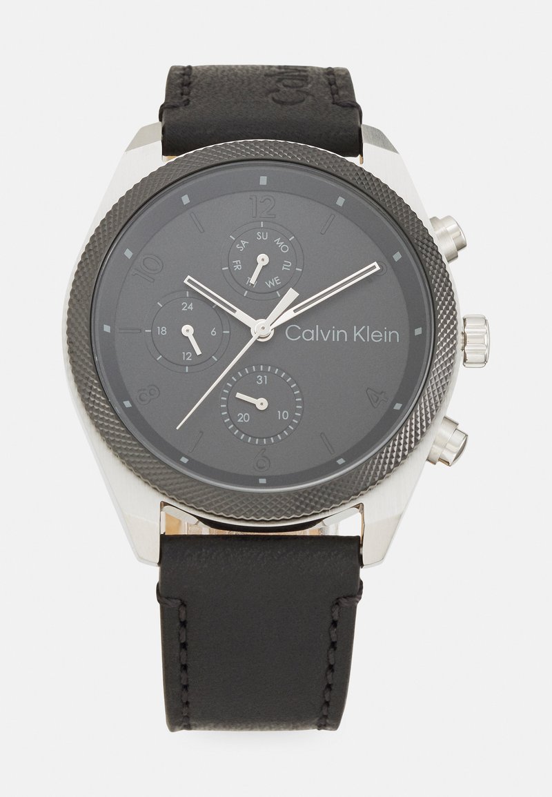 Montre avec bracelet en cuir noir, boîtier en acier inoxydable argenté, lunette texturée, cadran noir et index et aiguilles blancs.