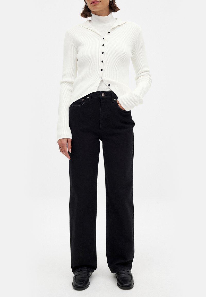 Valge ribaga nööpidega kardigan valge kõrge kaelusega särgi peal, millele on kombineeritud kõrge talje ja laiad mustad teksad ning mustad kingad.