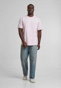 Light pink short-sleeve t-shirt paired with loose, faded blue jeans and white sneakers. Simple, relaxed design with a crew neck.