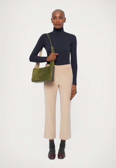 Marineblå turtleneck, beige skræddersyede bukser, grøn suede skuldertaske, grå sokker og tofarvede sko; minimalistisk design med neutral farvepalet.
