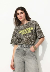 T-shirt à manches courtes imprimé léopard avec un texte graphique jaune. Associé à un jean en denim gris taille haute, affichant une coupe décontractée.