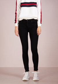 Svarta skinny jeans med hög midja, tillverkade av denim. Kombineras med en vit sweatshirt som har röda och marinblå ränder på ärmarna.