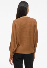 Pull marron à côtes avec une coupe décontractée, des épaules tombantes et des manches longues. La texture est douce et il a une longueur légèrement raccourcie.