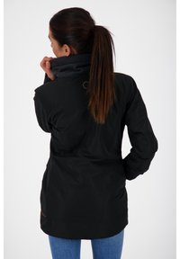 Musta ulkoilutakki, jossa on korkea kaulus ja harmaa vuori, tasaisella pinnalla ja logoyksityiskohdalla takana.