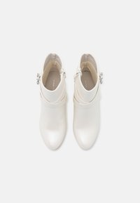 Botas blancas hasta el tobillo con punta afilada, textura de cuero suave, detalle de doble correa y herrajes de plata en el tobillo.
