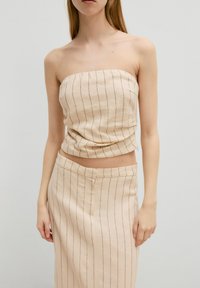 Strapless beige top met dunne verticale strepen, vervaardigd uit textuurstof. Gecombineerd met een bijpassende rok met een rechte snit en een eenvoudige tailleband.