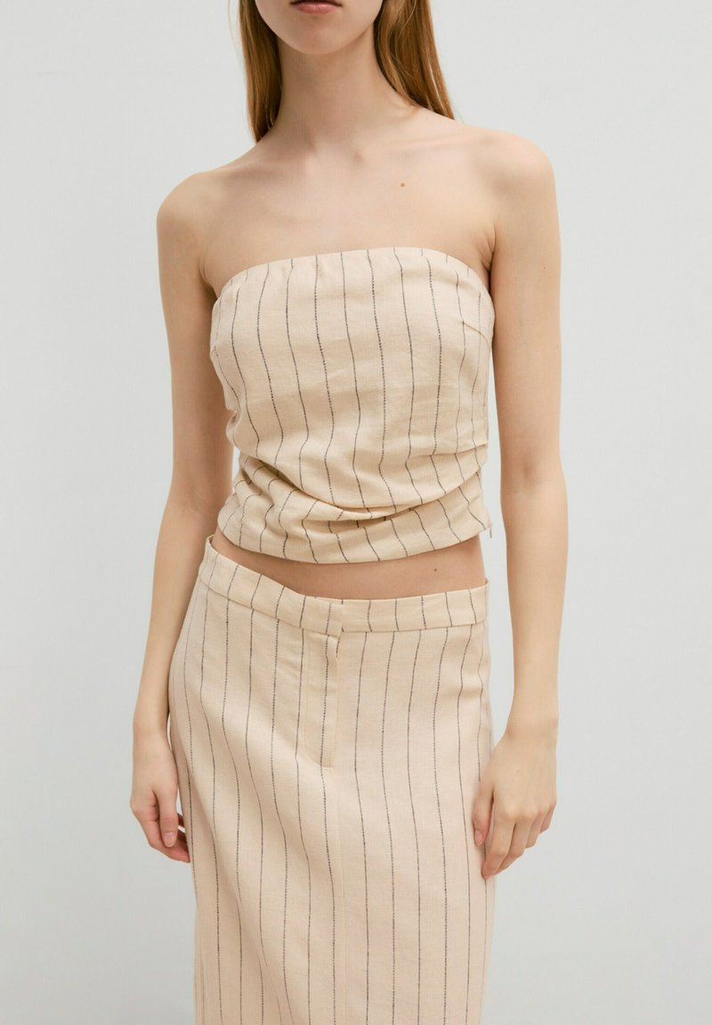 Strapless beige top met dunne verticale strepen, vervaardigd uit textuurstof. Gecombineerd met een bijpassende rok met een rechte snit en een eenvoudige tailleband.