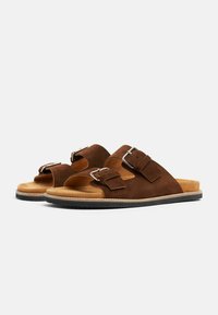 Smeđe nubuk sandale s dva podesiva kopčanja, mekanom unutrašnjošću i teksturiranom crnom gumenom potplatom. Dizajn s otvorenim prstima s minimalnim profilom.