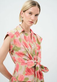 Blusa floreale in tessuto leggero con motivi di foglie rosa e verdi, maniche corte, colletto e cintura annodata in vita.