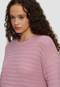 Jasnoróżowy sweter dzianinowy z poziomą fakturą rib, posiada okrągły dekolt i szerokie rękawy, prezentując miękki i przytulny wygląd.