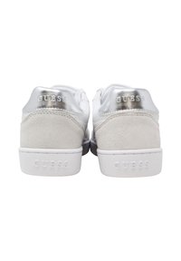 Un paio di sneakers bianche con accenti argentati sul tallone, pannelli in suede e "GUESS" impresso sui tab del tallone e sulle suole, viste da dietro.