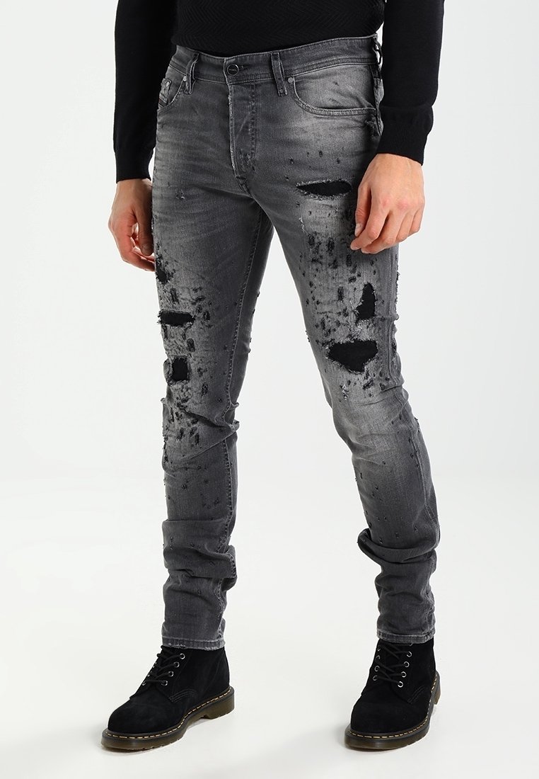 Šedé džíny s úzkým střihem, které mají distressed detaily, roztržení a vybledlou texturu. V kombinaci s černými semišovými kotníkovými botami.